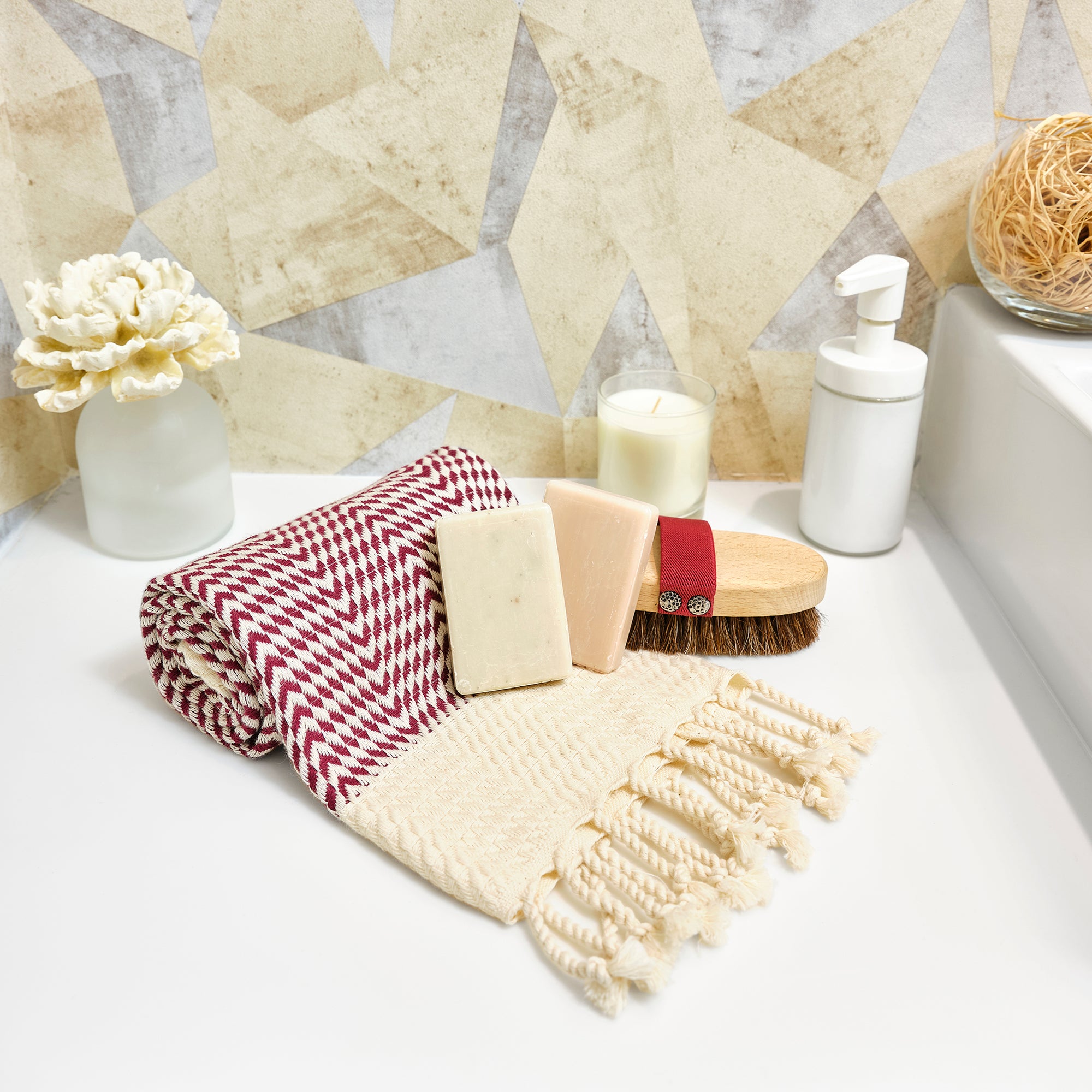 Bath products including a checkered towel, soap, and brush on a bathroom counter with a geometric tile pattern.