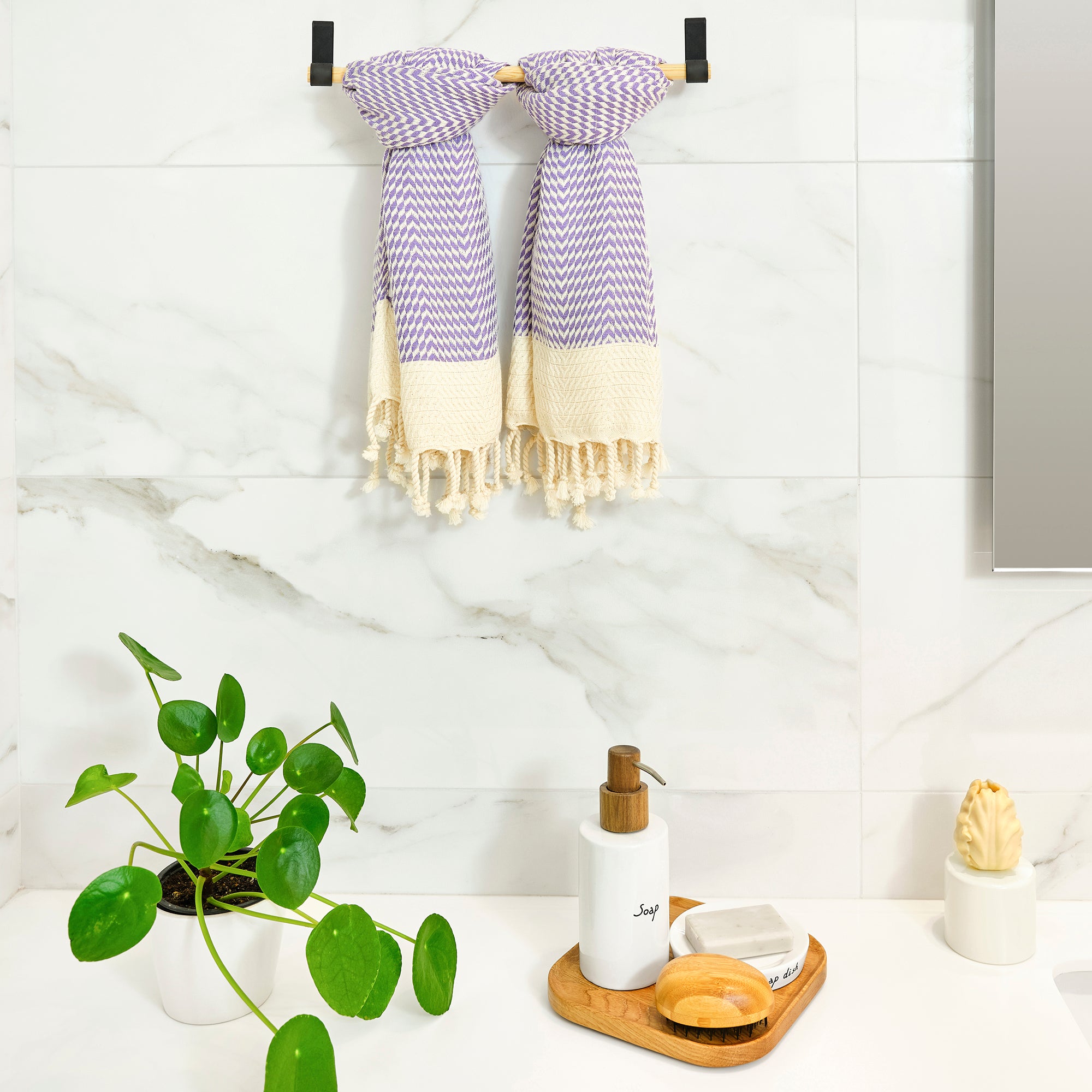 Towel rack with striped towels, plant, and bathroom items on a white tiled wall.